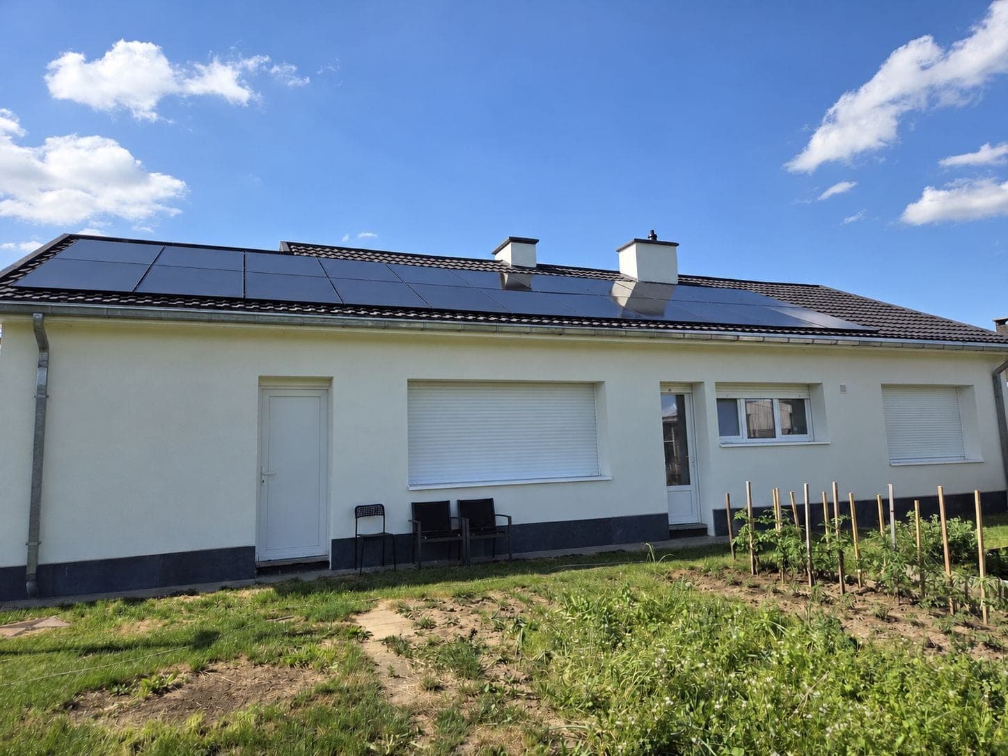 Single-storey white house seen from the garden, with rows of full-black solar panels across its tiled roof and two chimneys