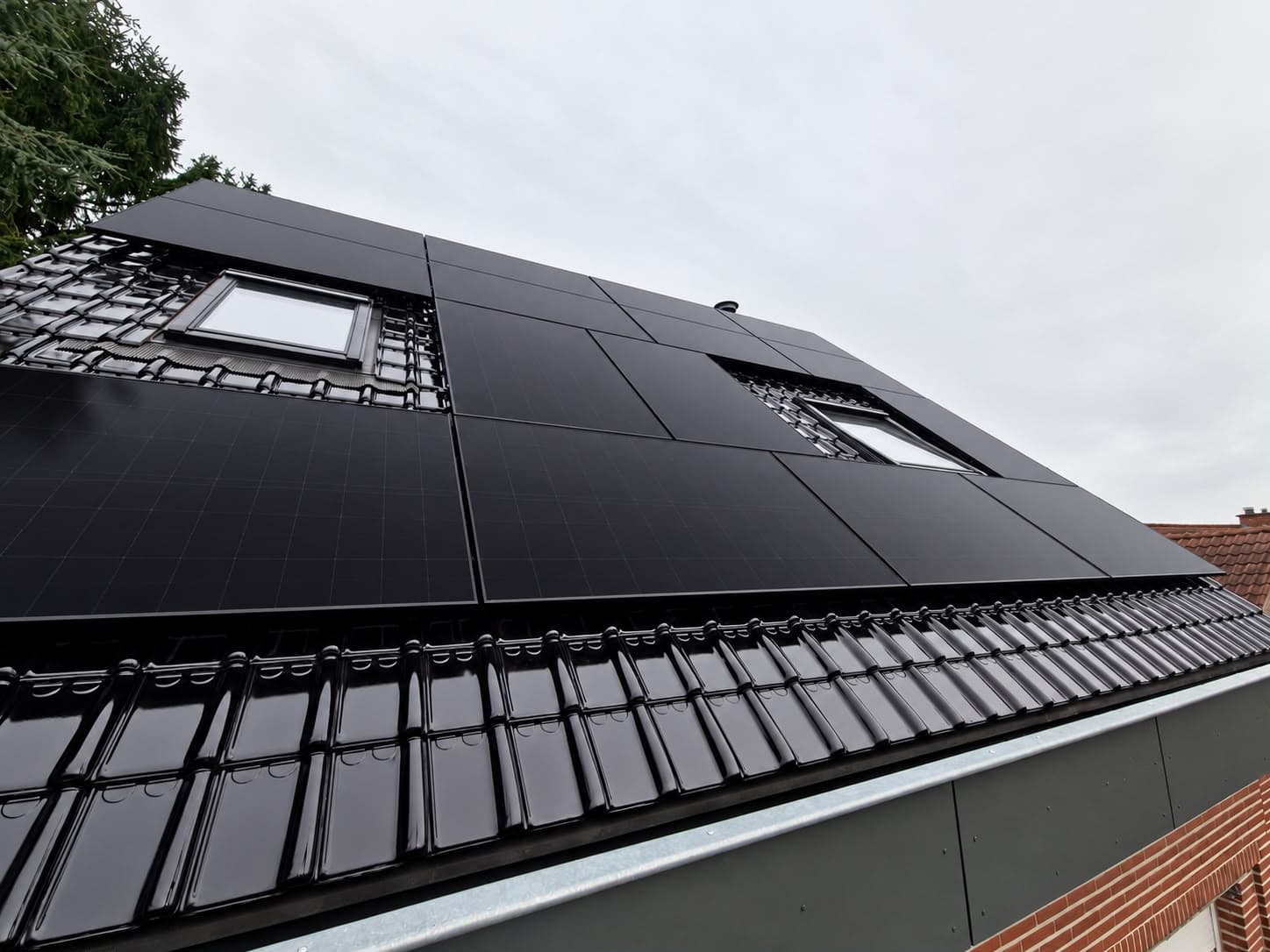 Black solar panels on a tiled roof behind a garden hedge